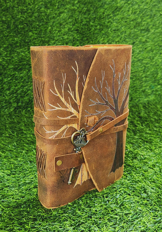 Brown leather journal with tree design and key charm on a green grass background