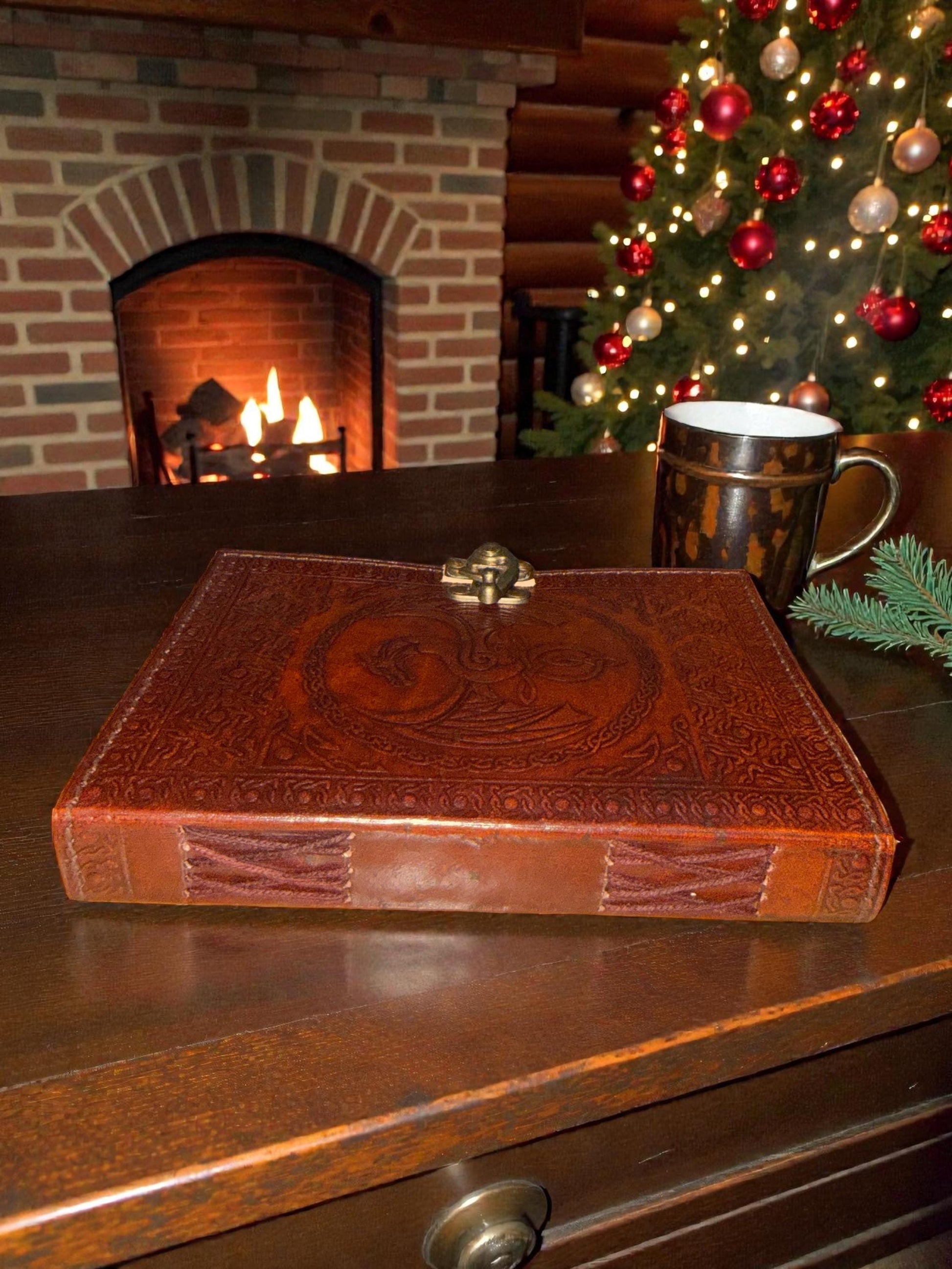 Brown leather-bound book on a wooden surface with a Christmas tree and fireplace in the background
