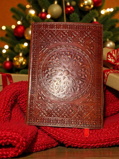 Decorative brown leather notebook on a red blanket with a Christmas tree in the background